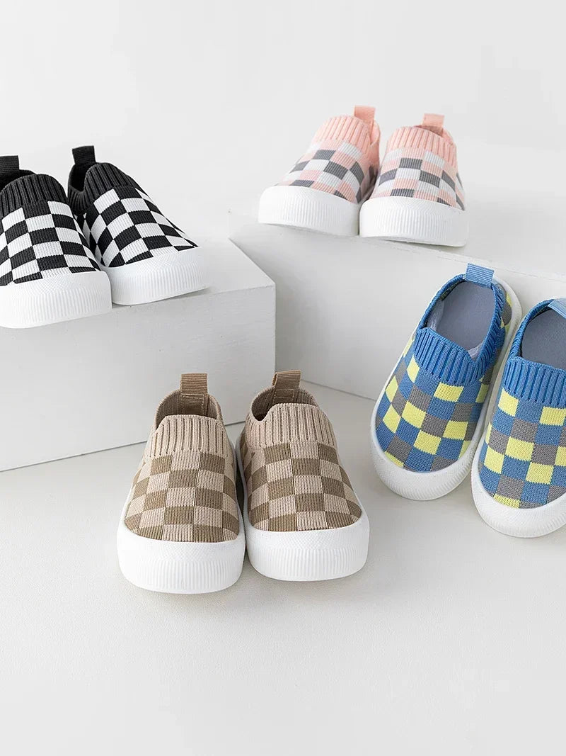 A collection of plaid slip-on toddler shoes in pink, black, and yellow checkered patterns displayed on a white surface.