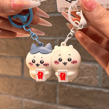 A pair of cute cartoon bear keychains, one blue and one white, are held by a hand against a brick background.