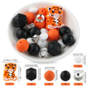 A white bowl filled with various orange and black silicone beads shaped like a tiger, including round, flat, and ring-shaped 