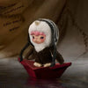 A small plush doll with pink hair and white fur is placed on a red dish against a beige background.