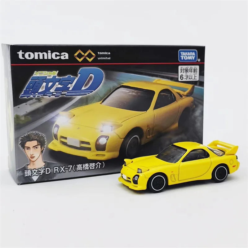 A yellow Tomica die-cast sports car model, the D RX-7, displayed next to its packaging.