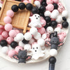 A collection of pink and black silicone crafting beads arranged on a white plate with a wooden grid background.