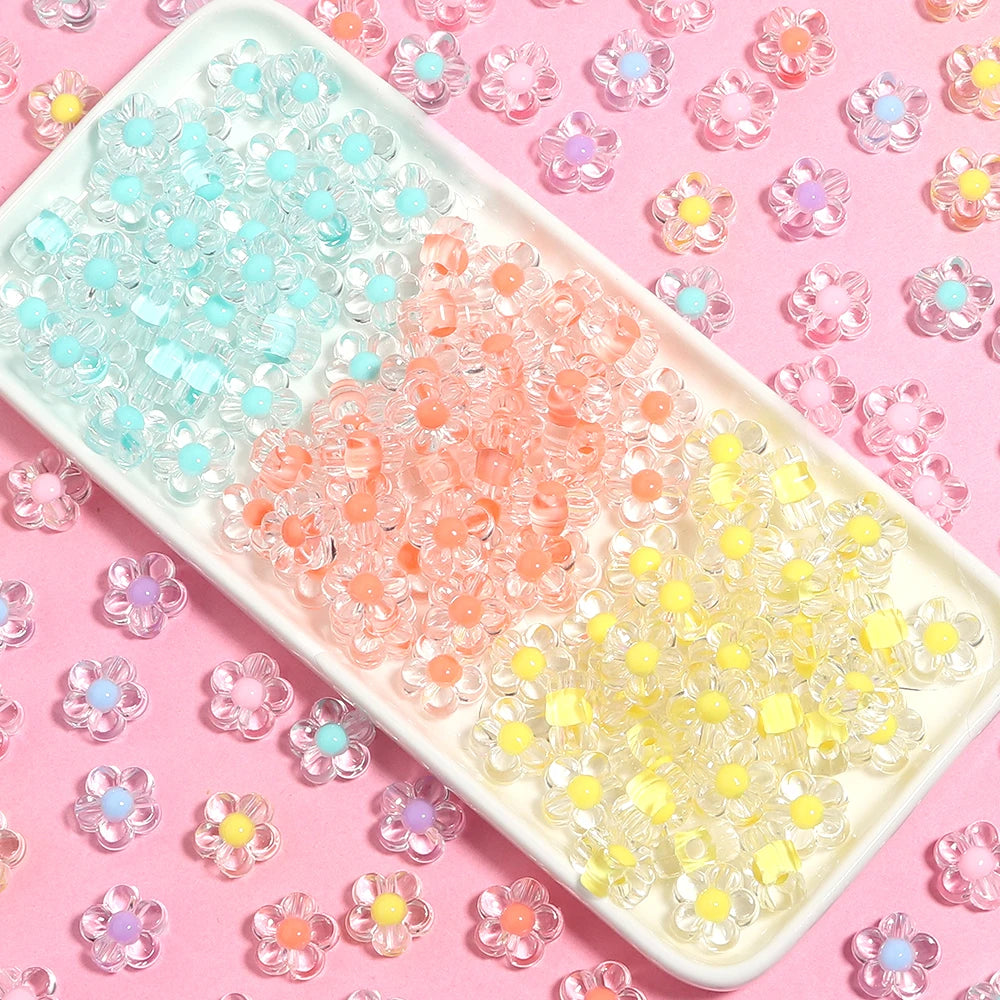 A rectangular tray filled with colorful transparent acrylic flower beads in shades of blue, pink, and yellow on a pink backgr
