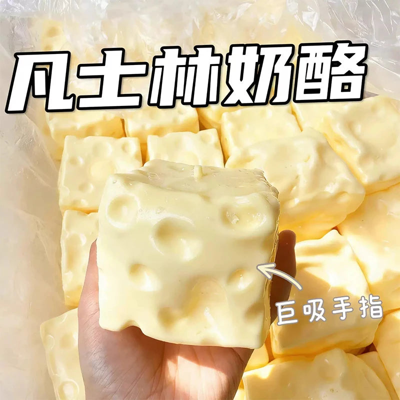 A hand holds a yellow squishy cheese cube stress ball with dimples, surrounded by other similar cubes.