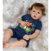 A realistic reborn toddler doll with rooted hair lying on a white fluffy surface.