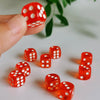 A hand holds a red and white polka dot die, with several other orange dice scattered on a white surface.