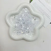 A white, flower-shaped dish filled with clear acrylic ice strips for nail art and DIY crafts.
