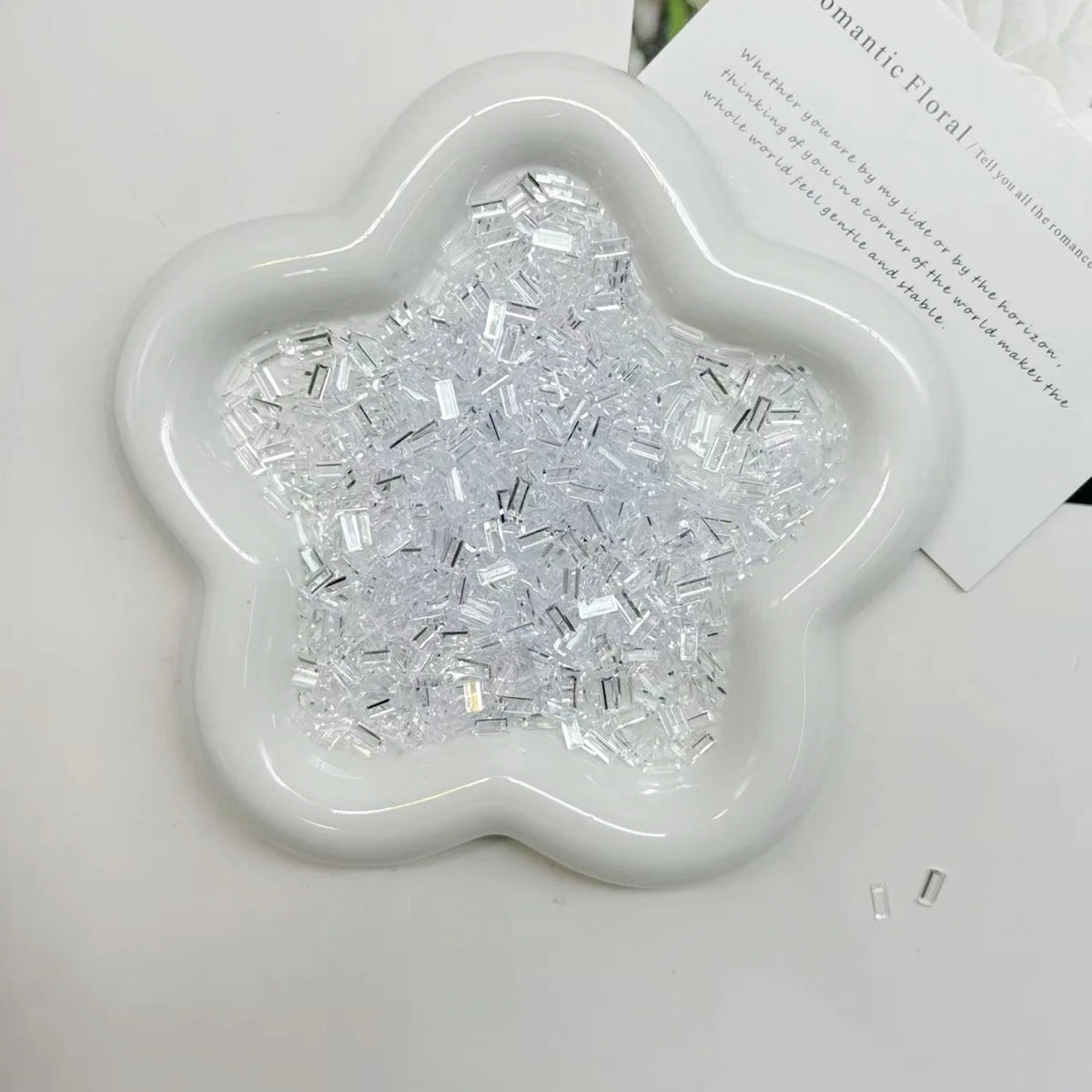 A white, flower-shaped dish filled with clear acrylic ice strips for nail art and DIY crafts.