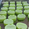 A tray of light green cat and cheese squishy stress-relief toys arranged in a grid.