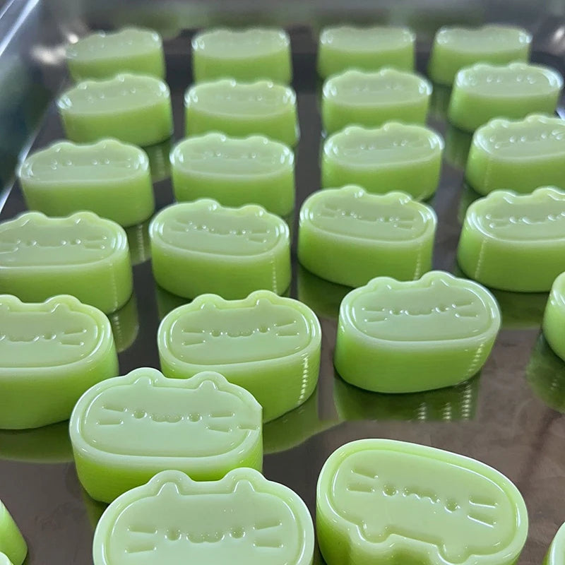 A tray of light green cat and cheese squishy stress-relief toys arranged in a grid.