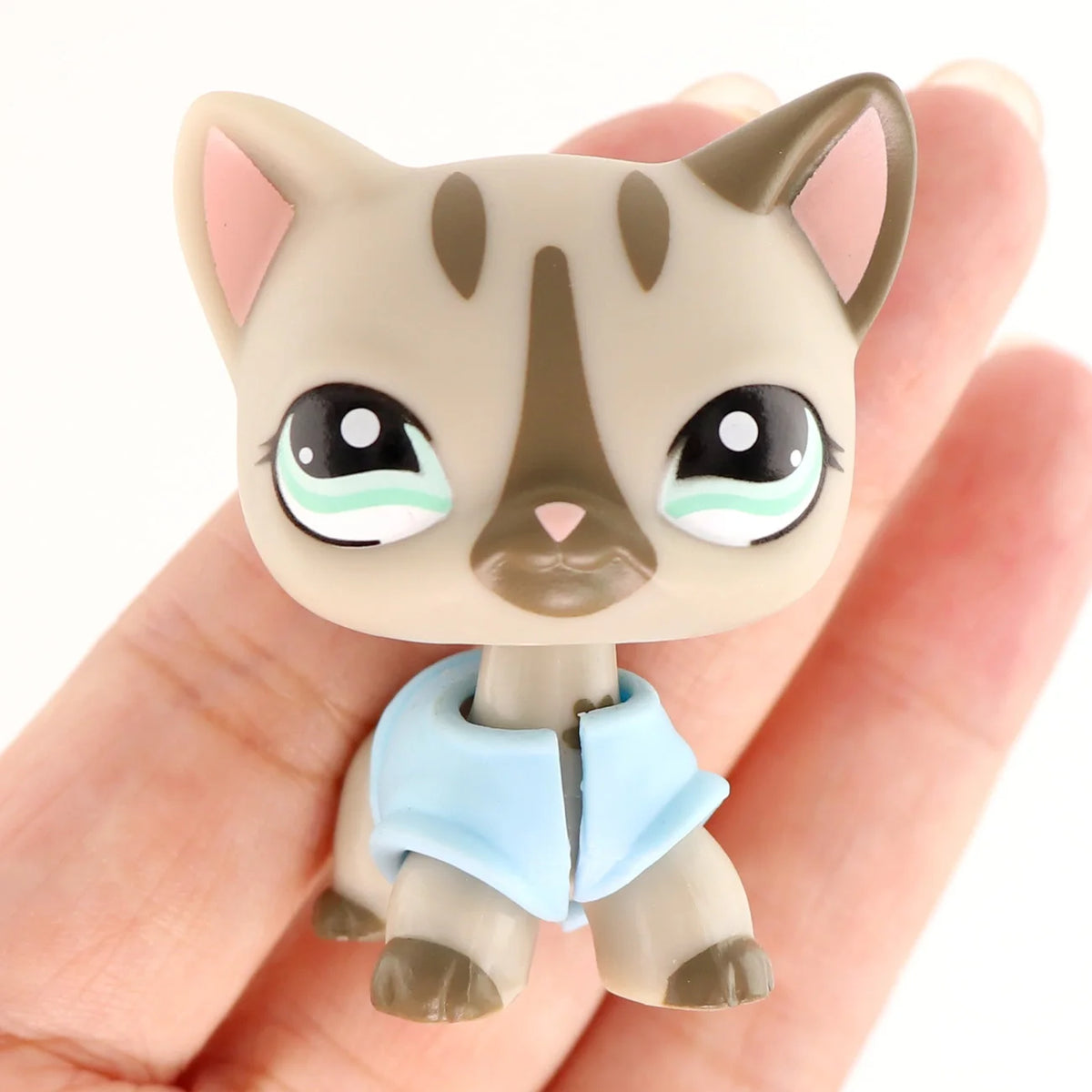 A small, light brown cat figure wearing a light blue collar is held in a person's hand.