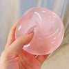 A hand holds a translucent pink squishy stress relief fidget toy against a light background.
