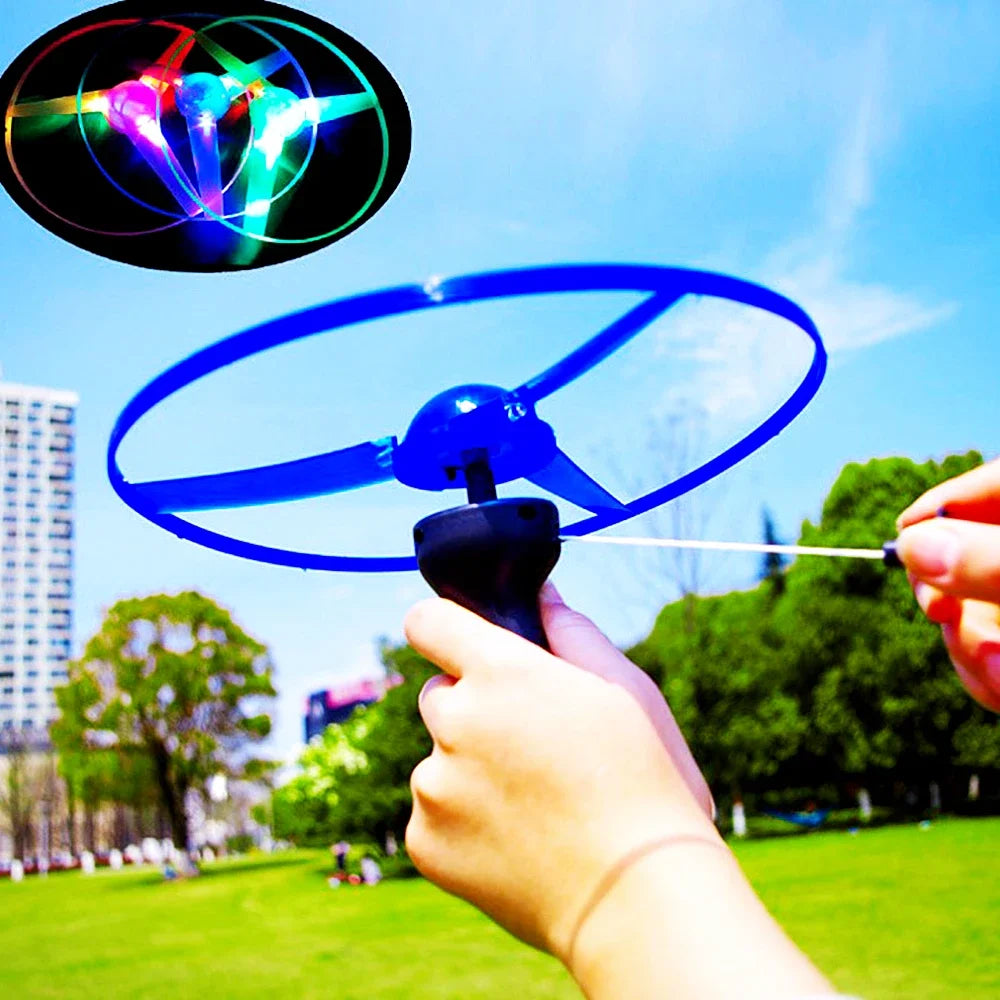 A hand holds a blue spinning disc toy with a pull string, demonstrating its flight capability against a bright sky.