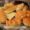 A variety of realistic bread-shaped toys and food items are displayed on a wooden surface.