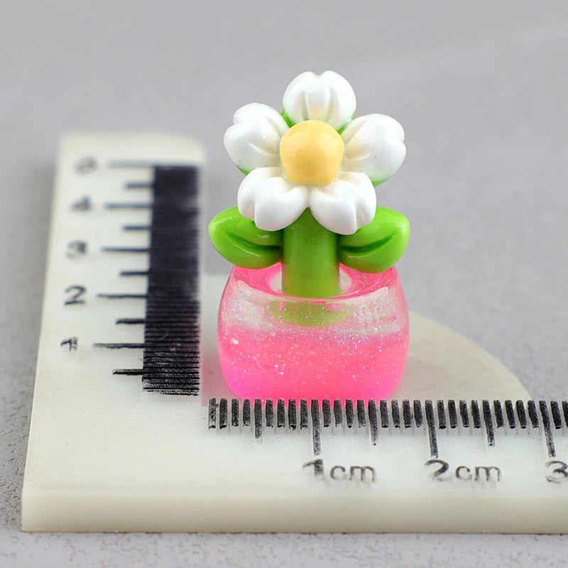 A miniature white flower in a green pot is placed on a ruler showing measurements.