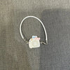 A white necklace with a small camera charm and pink accents displayed on a gray fabric background.