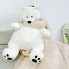A white plush polar bear stuffed animal sitting on a light fabric surface.