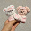 A pair of pink and white cartoon animal plush keychains being held in a hand.