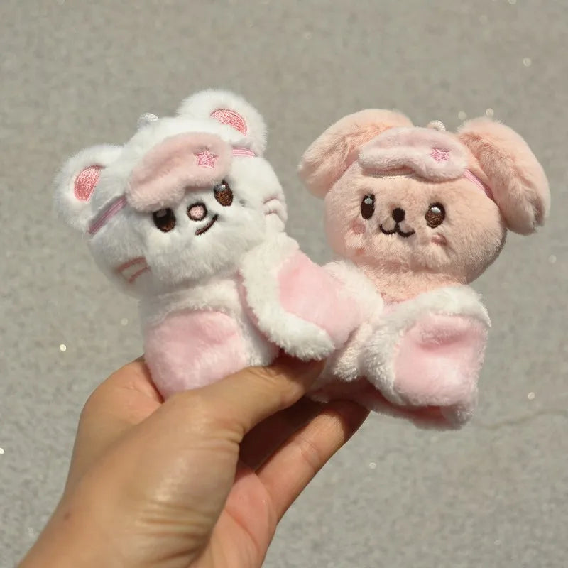 A pair of pink and white cartoon animal plush keychains being held in a hand.