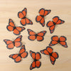 Collection de monarques oranges avec marques noires, disposés sur une surface en bois clair.