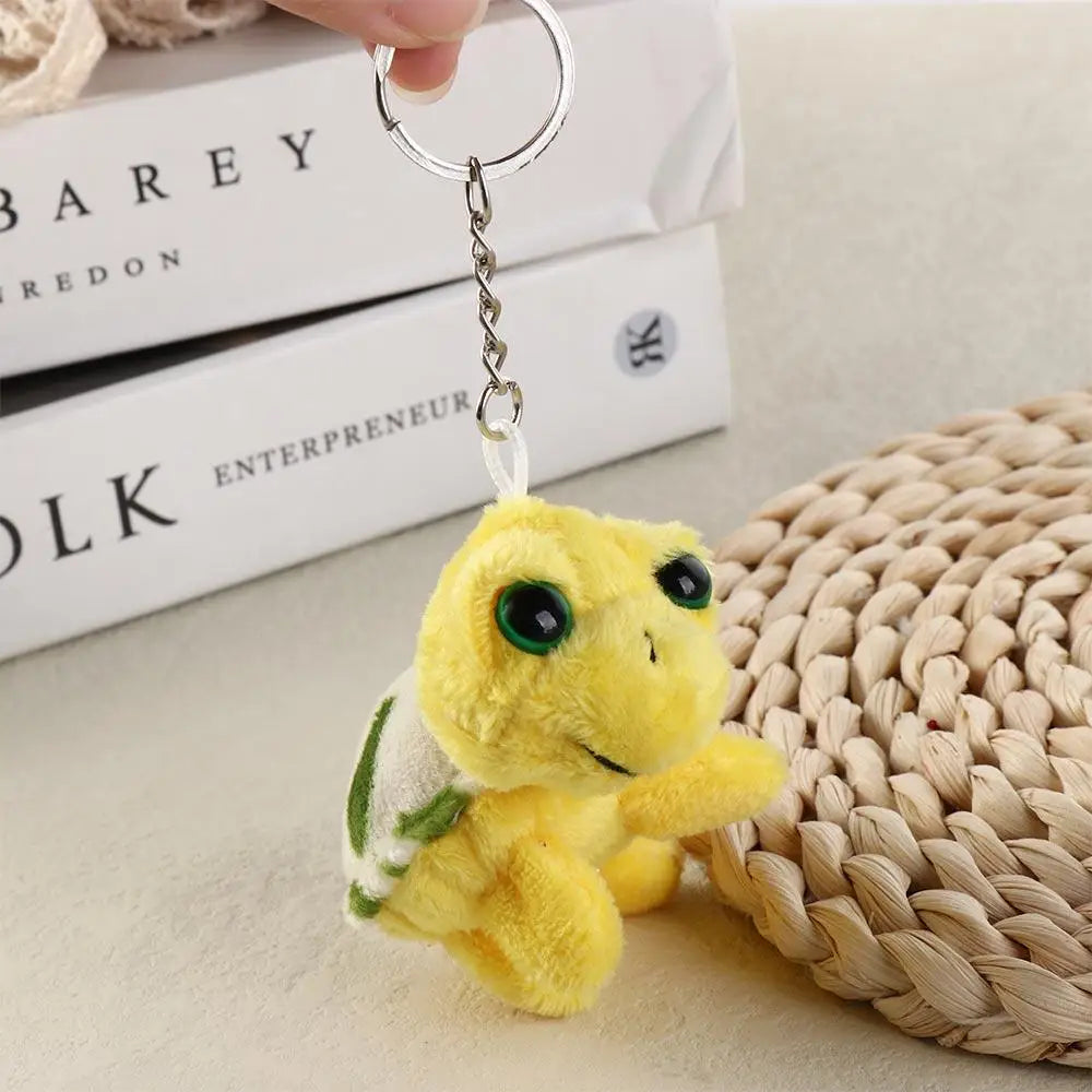 A yellow turtle plush charm attached to a silver keyring, resting on a woven mat next to stacked books.