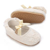 A pair of light beige lace-trimmed baby girl moccasin shoes with a satin bow