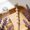 A light wood tray holds a baby pacifier clip with a burlap flower design and lavender sprigs.