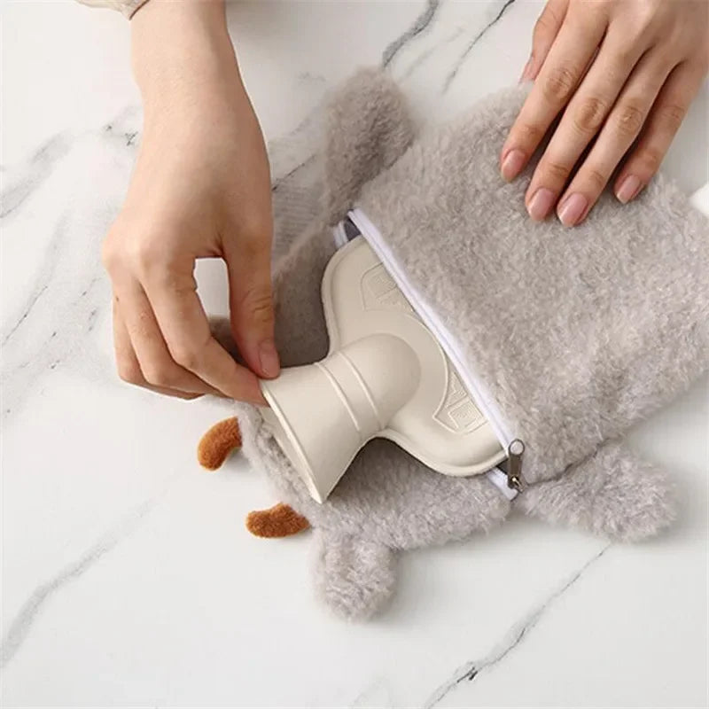 A hand is holding a light beige plush-covered hot water bottle with a zipper on a marble surface.