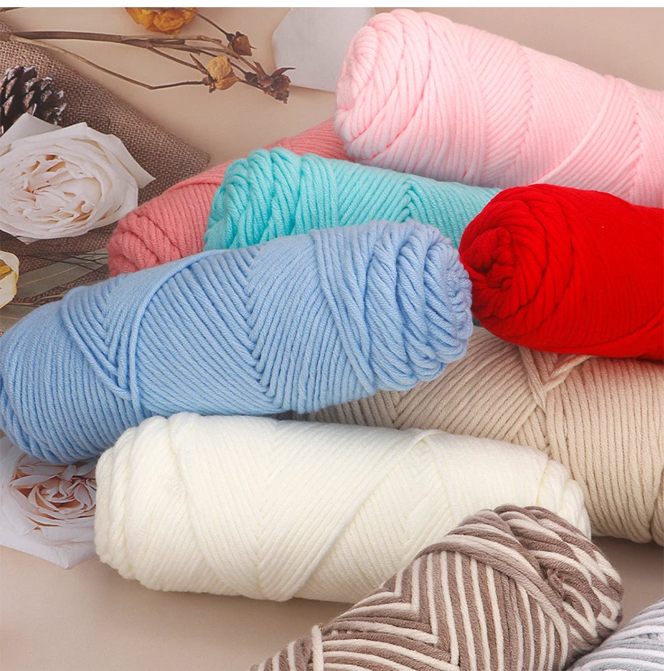 A collection of three skeins of soft cotton blend yarn in various pastel and bright colors like pink, blue, red, and cream.