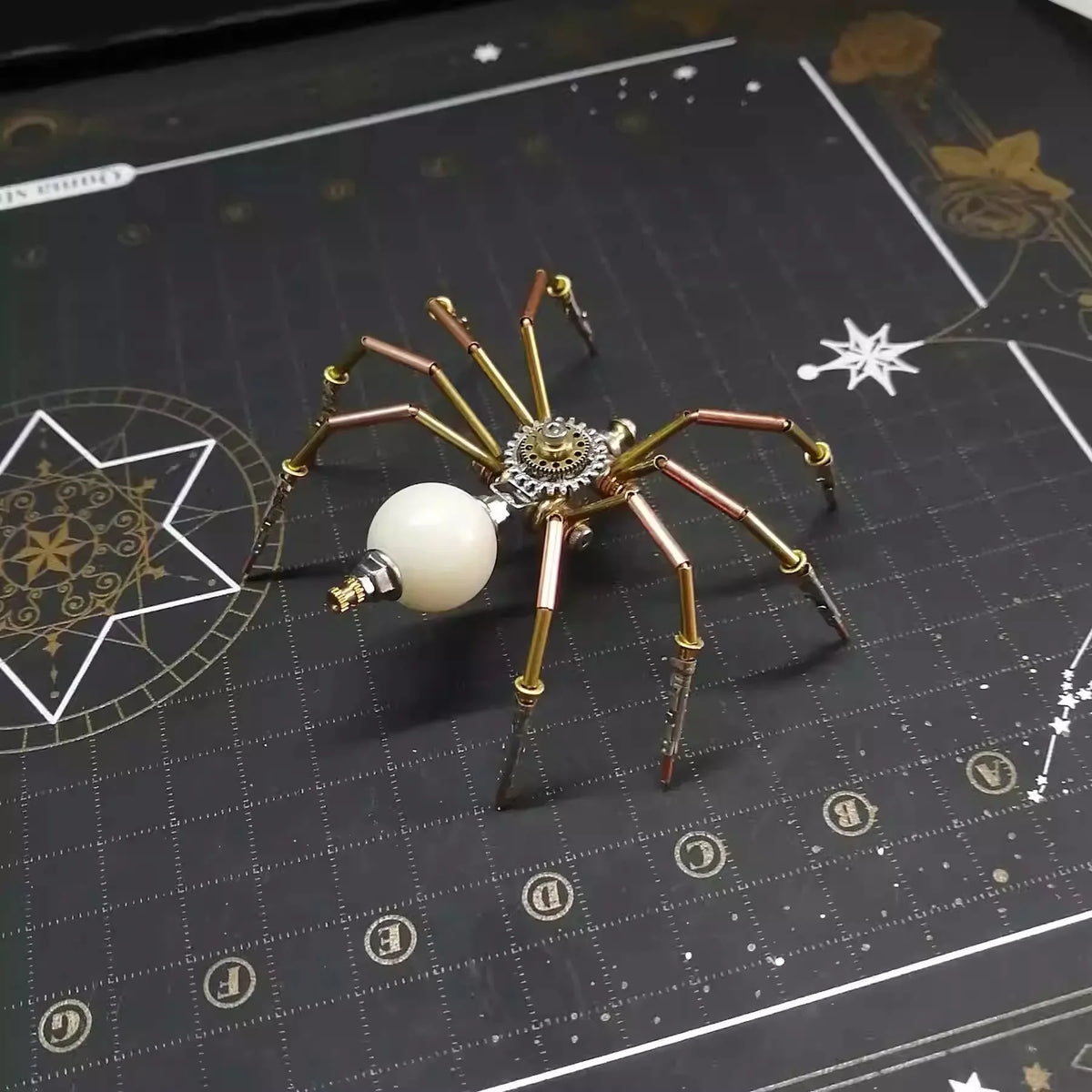 A detailed steampunk metal spider puzzle assembly kit with gold and copper colored legs and a white sphere.