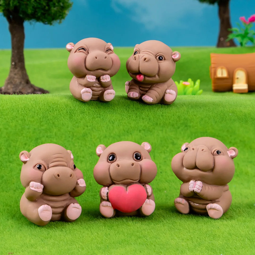 Three small, round, pinkish-brown resin hippo figurines sitting on green grass.