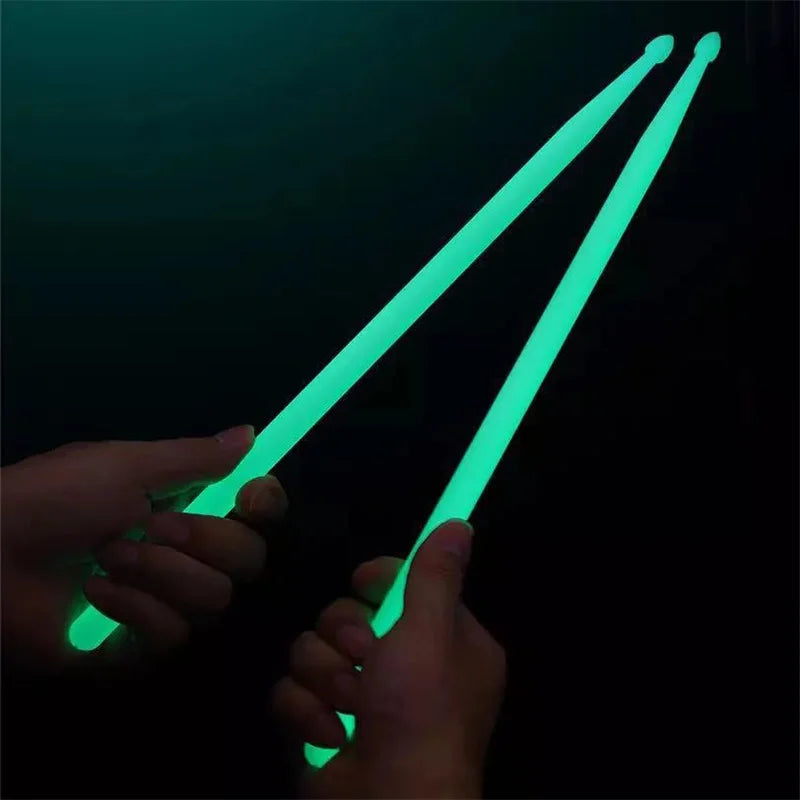 A hand holds a pair of bright green glow-in-the-dark nylon drumsticks against a dark background.