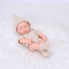 A realistic soft vinyl baby doll with a newborn outfit set wearing a knitted hat and clothing, lying on white fur.