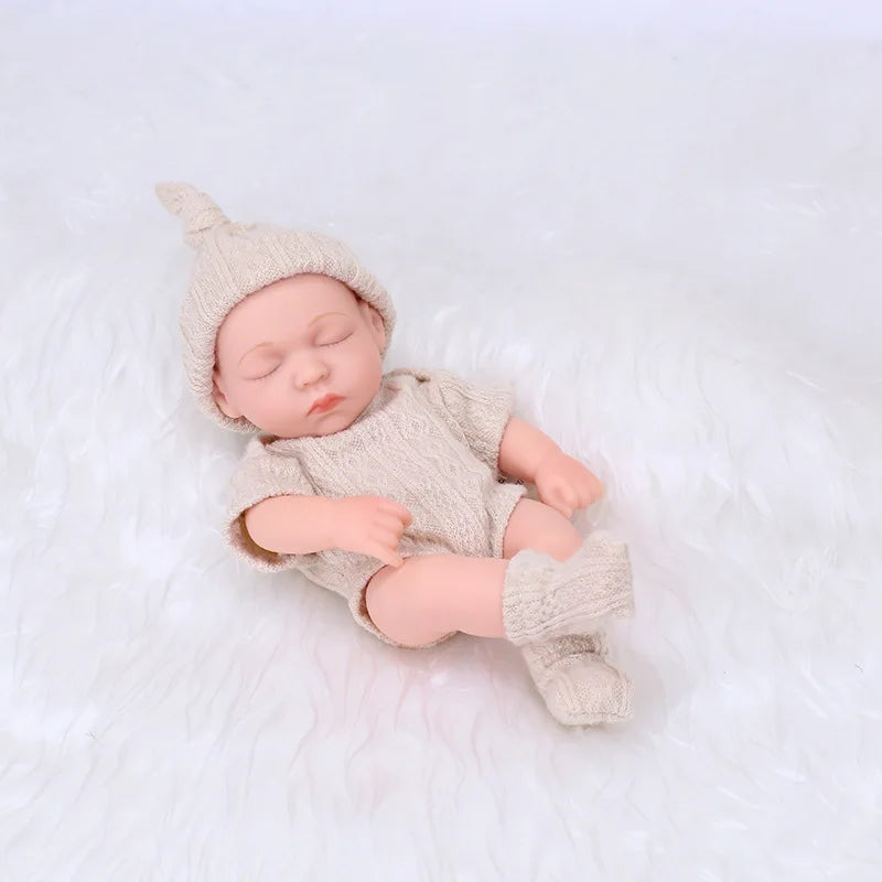 A realistic soft vinyl baby doll with a newborn outfit set wearing a knitted hat and clothing, lying on white fur.