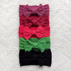 A stack of five colorful fabric bow baby headbands in shades of pink, red, coral, green, and black.