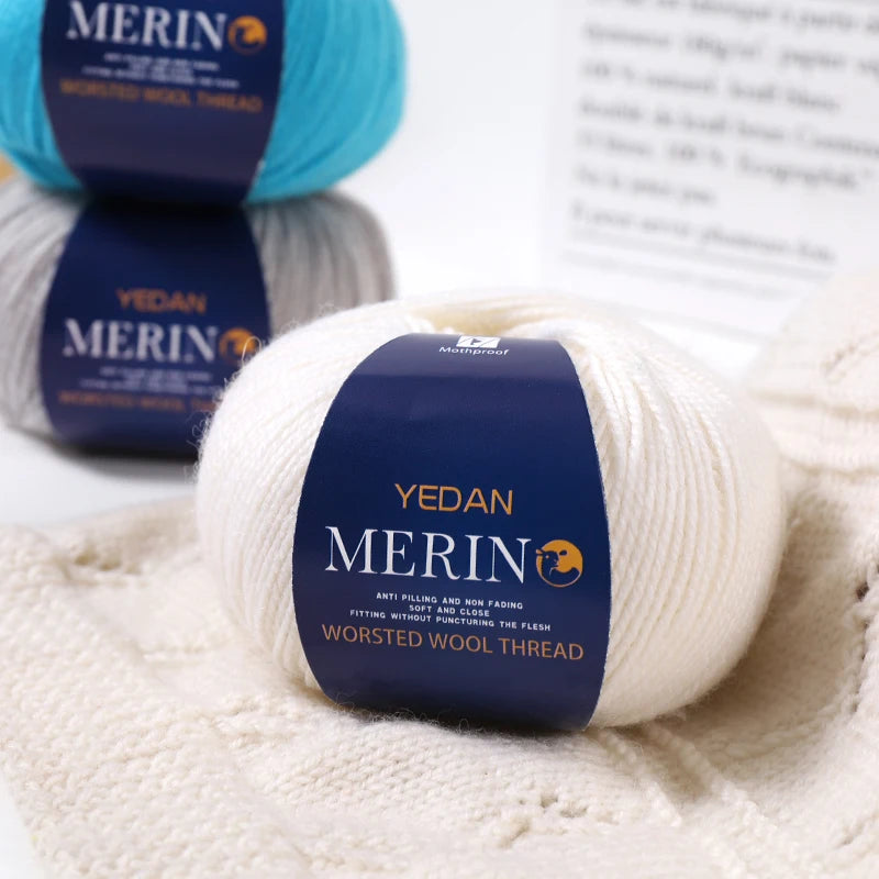 White YEDAN MERINO wool thread skeins resting on a cream-colored knitted fabric.