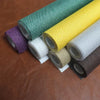 Rolls of linen book binding cloth in various colors including green, yellow, purple, and beige on a brown surface.