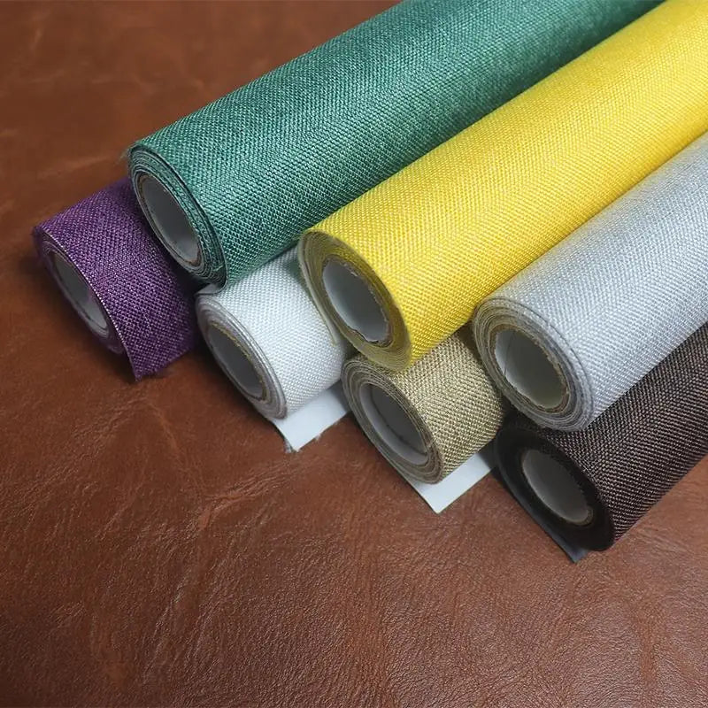 Rolls of linen book binding cloth in various colors including green, yellow, purple, and beige on a brown surface.
