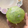 A hand holds a translucent lime green stress ball with small glittery stars and an apple design against a blurred background.