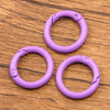 Four purple metal O-ring spring clasps arranged on a wooden surface.