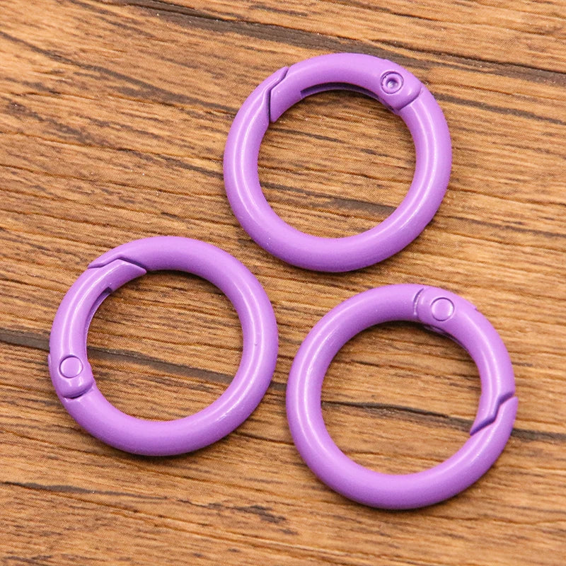 Four purple metal O-ring spring clasps arranged on a wooden surface.