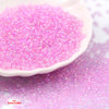 A pile of bright pink glossy glass seed beads spread on a white surface.