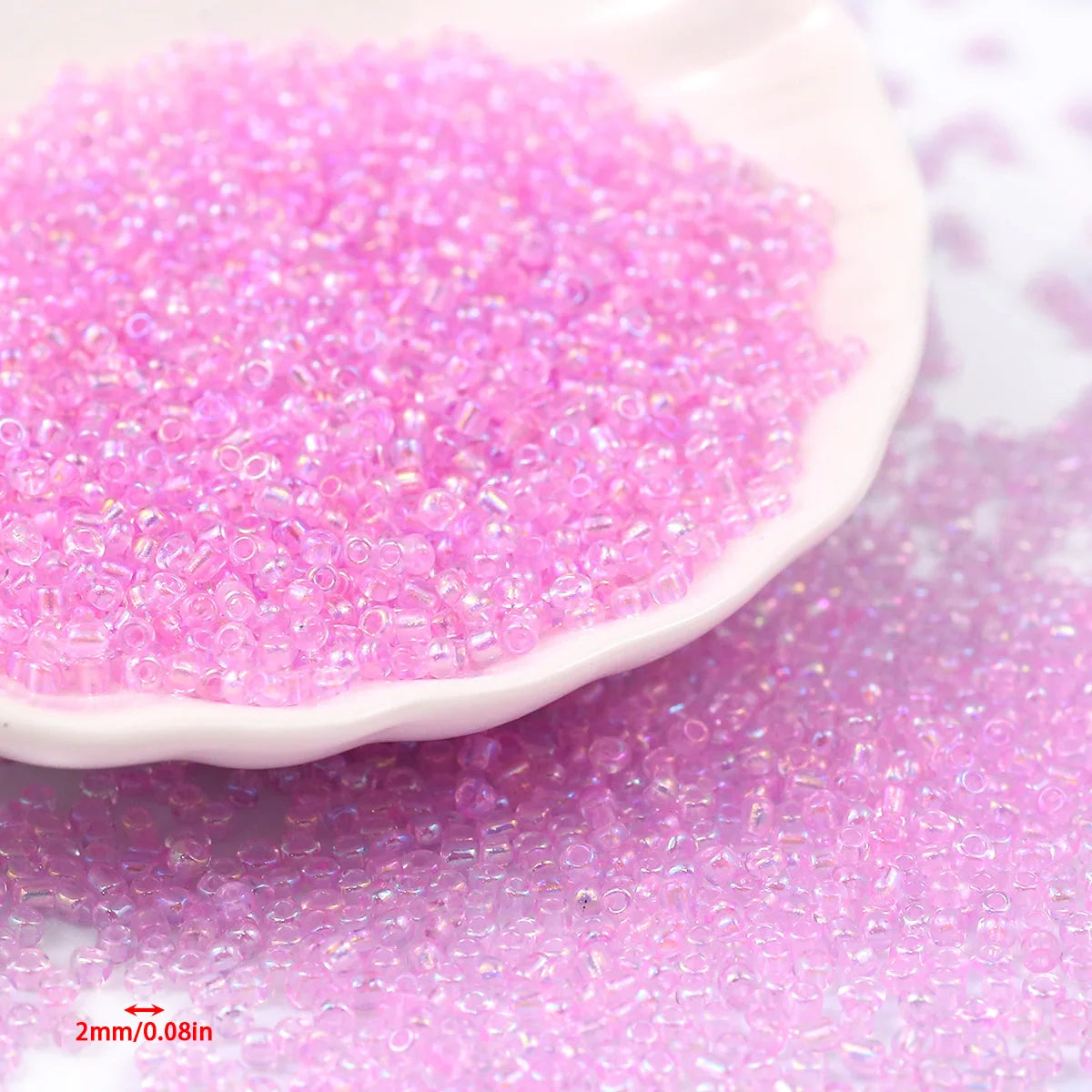 A pile of bright pink glossy glass seed beads spread on a white surface.