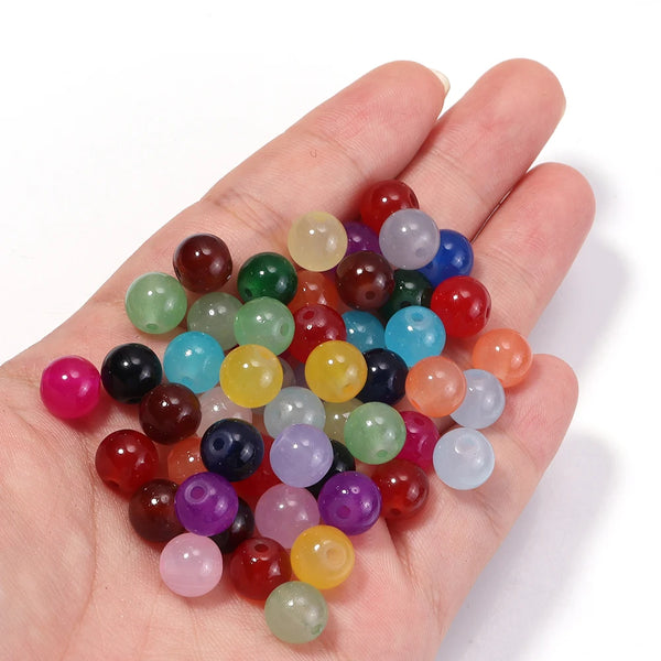 A hand holds a collection of round glass spacer beads in various colors and shades for jewelry making