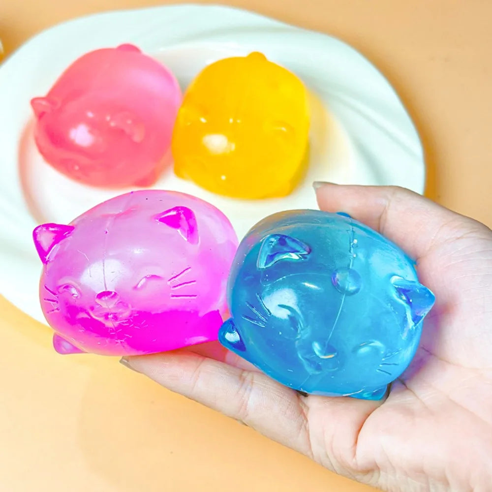 Three colorful cat squishy toys in pink, yellow, and blue are held in a hand.