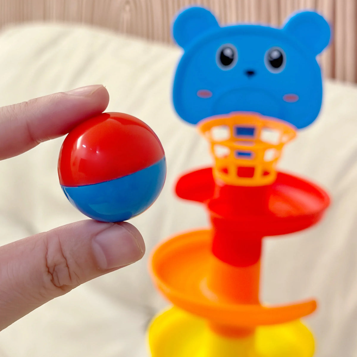 A hand holds a blue and red ball tower with a cat-shaped top and an orange drop mechanism.