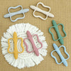 A collection of silicone teethers in various pastel colors and textures arranged on a beige fabric.
