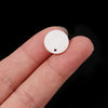 A hand holds a natural white shell bead with a round disc shape and a small hole.
