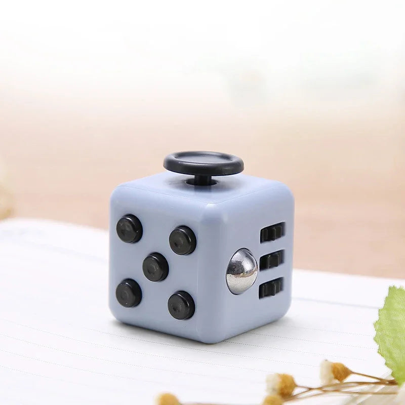 A light blue fidget cube with a rotating joystick and magnetic buttons resting on a white surface.
