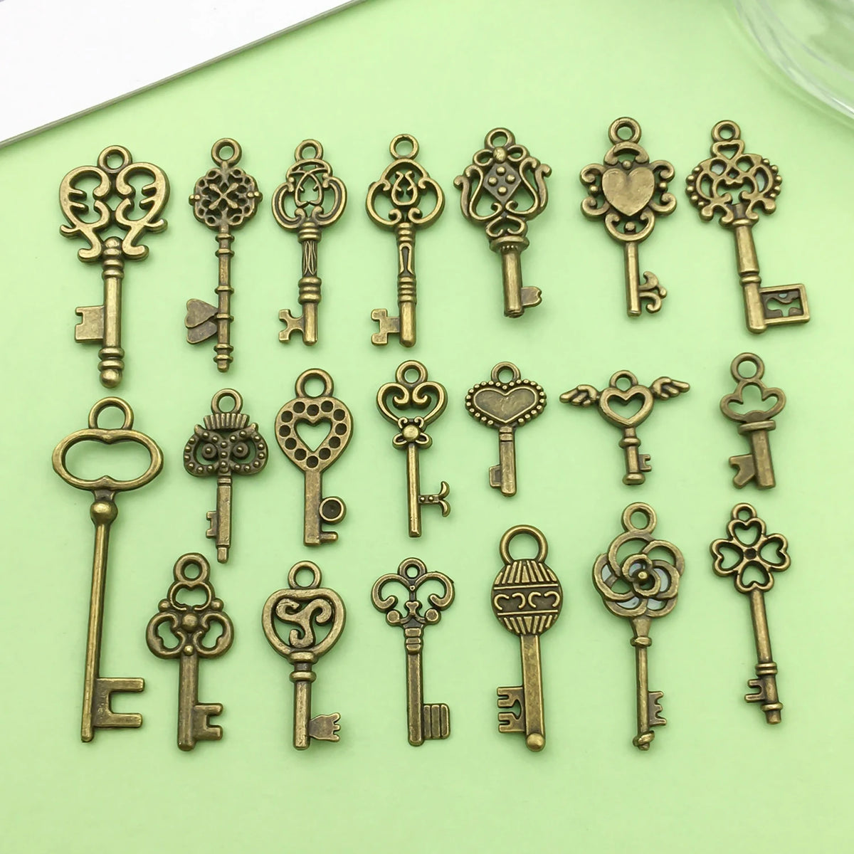 A collection of vintage brass key charms for jewelry making displayed on a light green surface.
